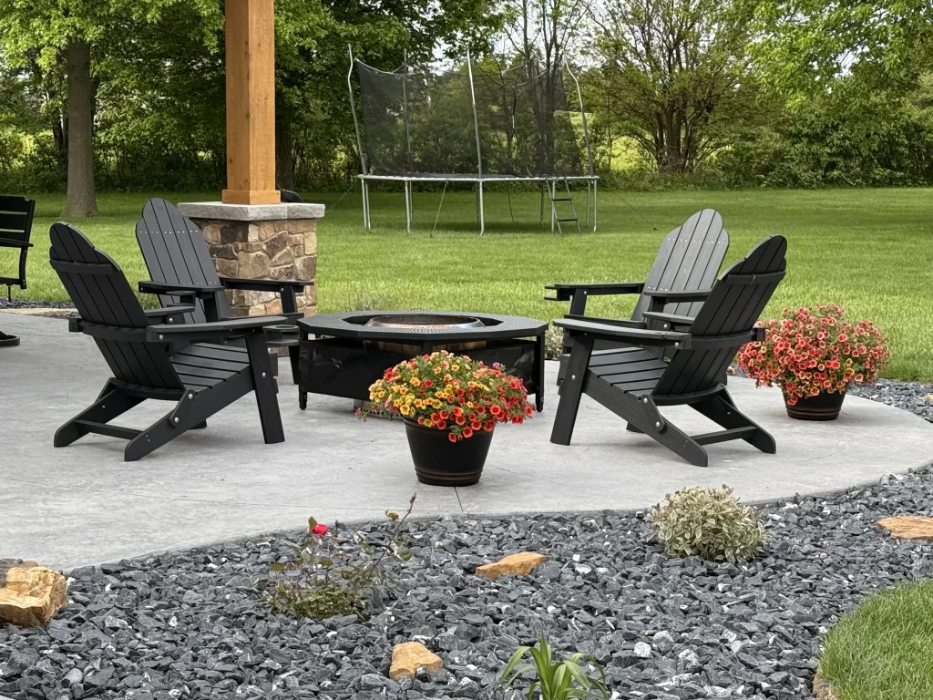 Backyard fire pit surrounded by Adirondack chairs and flowers