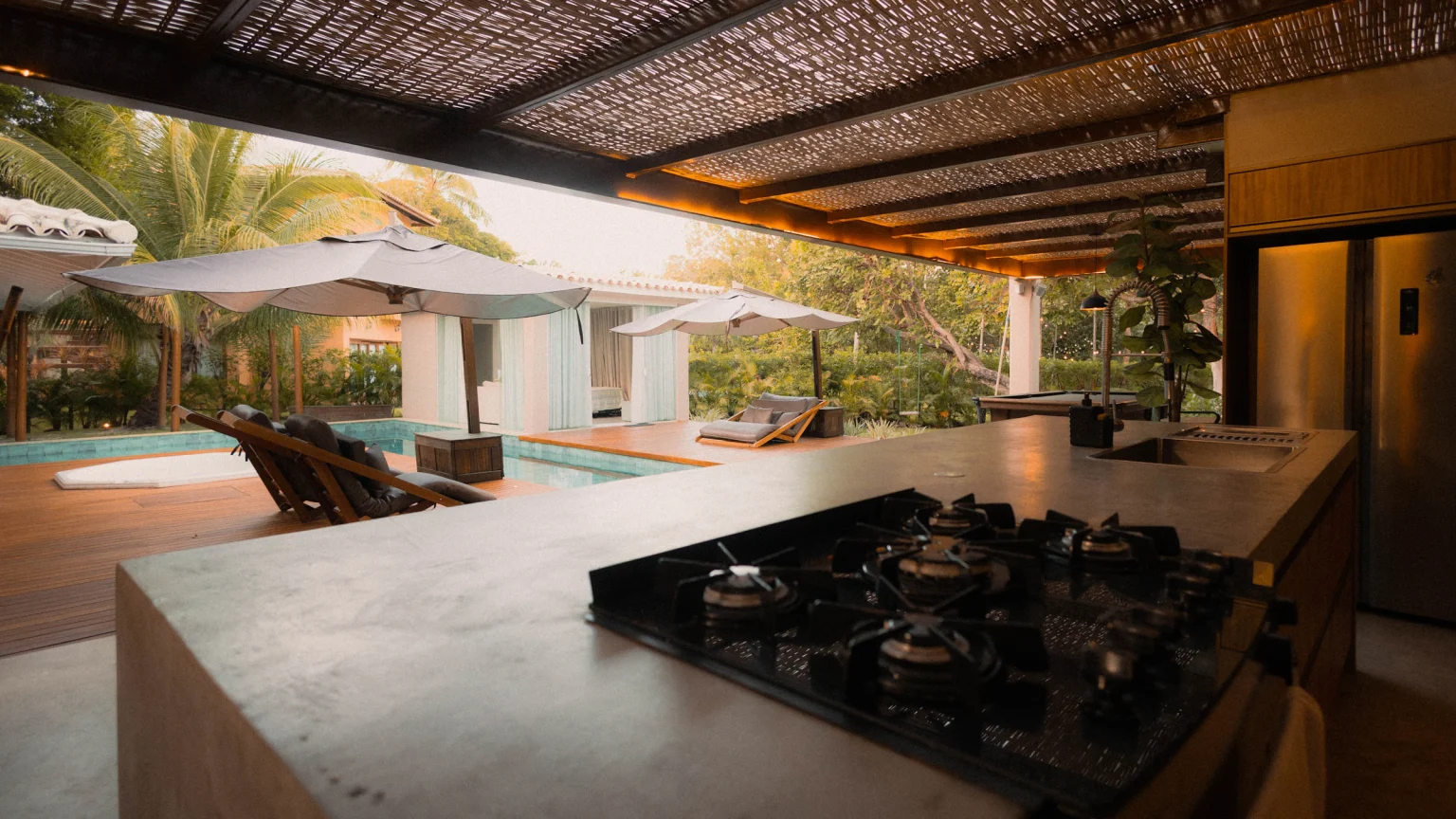 Modern outdoor kitchen with counters and seating next to a pool