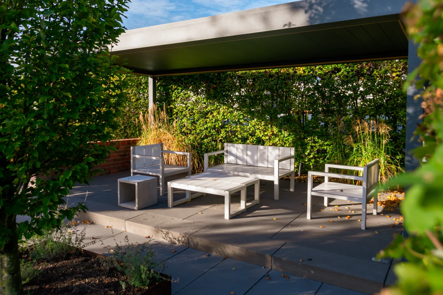 Modern outdoor lounge with white furniture under a shaded roof