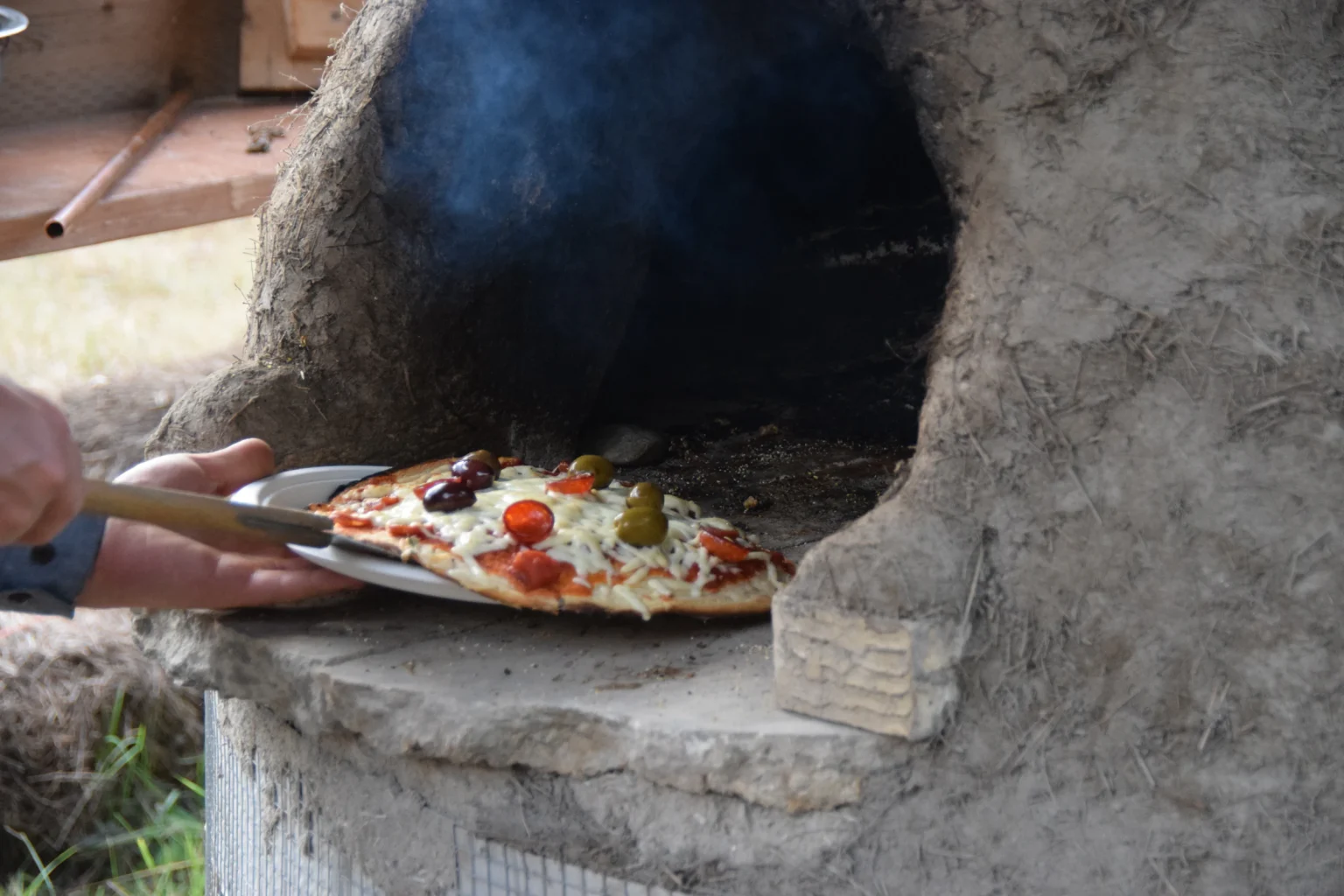 Pizza being placed into an outdoor wood-fired oven