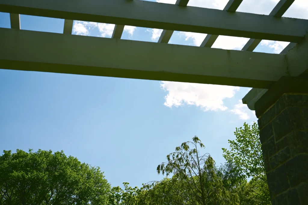 Pergola beams framed against a blue sky and green trees