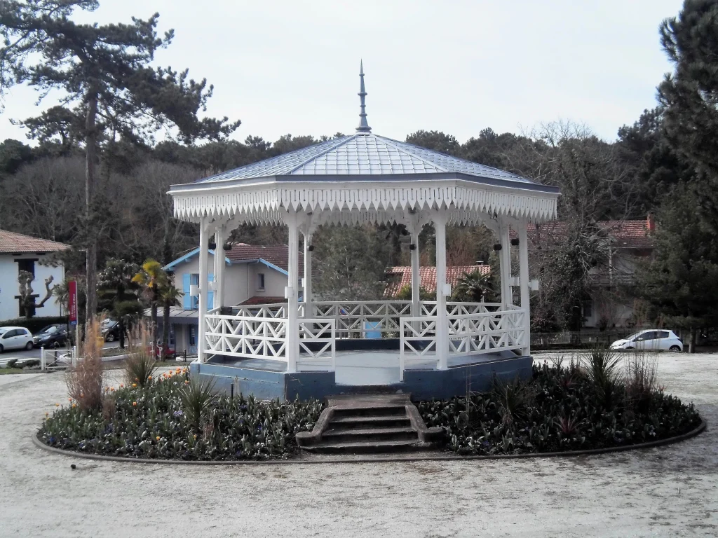White wood gazebo with a metal roof in a landscaped garden