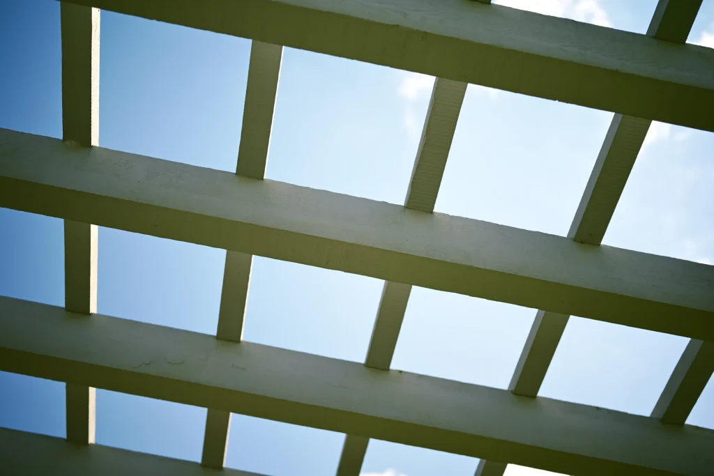 Detail of wood pergola rafters and trellis against a clear sky